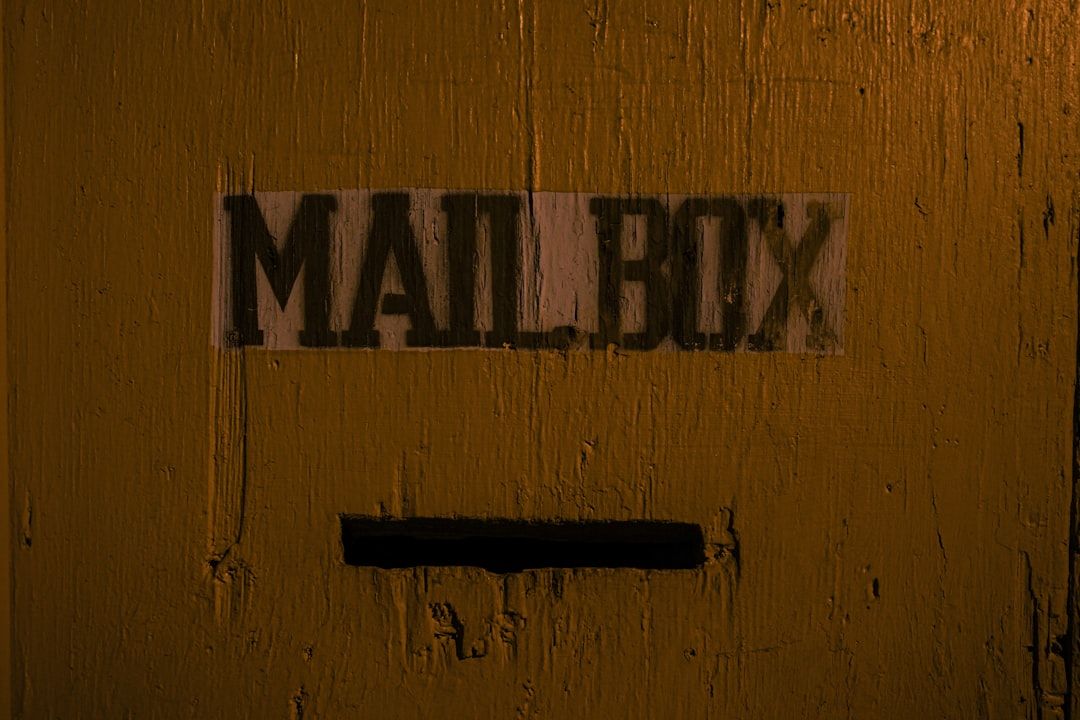 En postlådeöppning på en gul trävägg med texten "MAILBOX" ovanför.