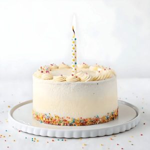 En liten vit tårta med strössel och ett brinnande ljus, perfekt för fotografering.